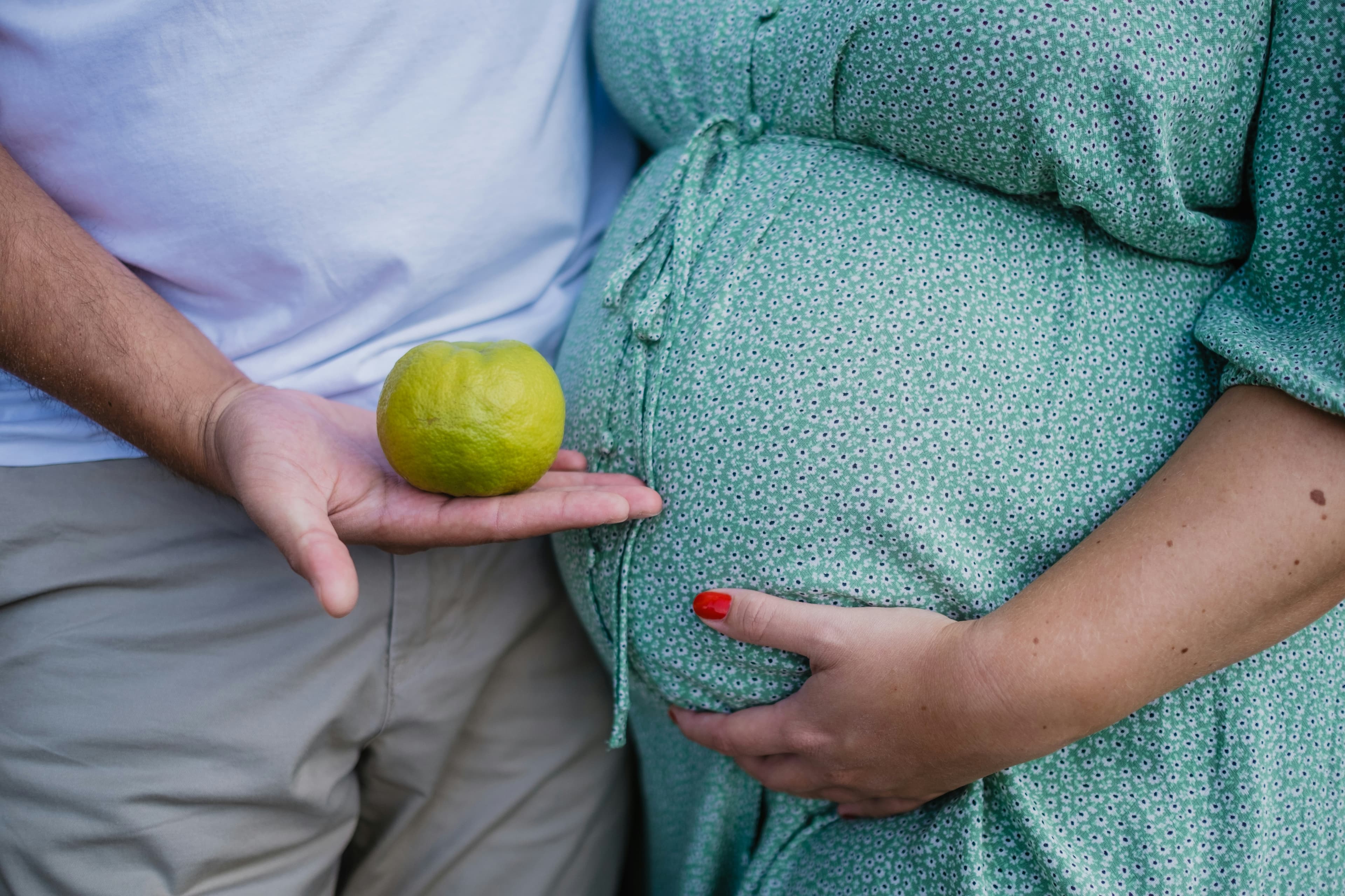 Pregnant woman holding fruit next to her belly — baby size comparison — Photo by Filipp Romanovski on Unsplash